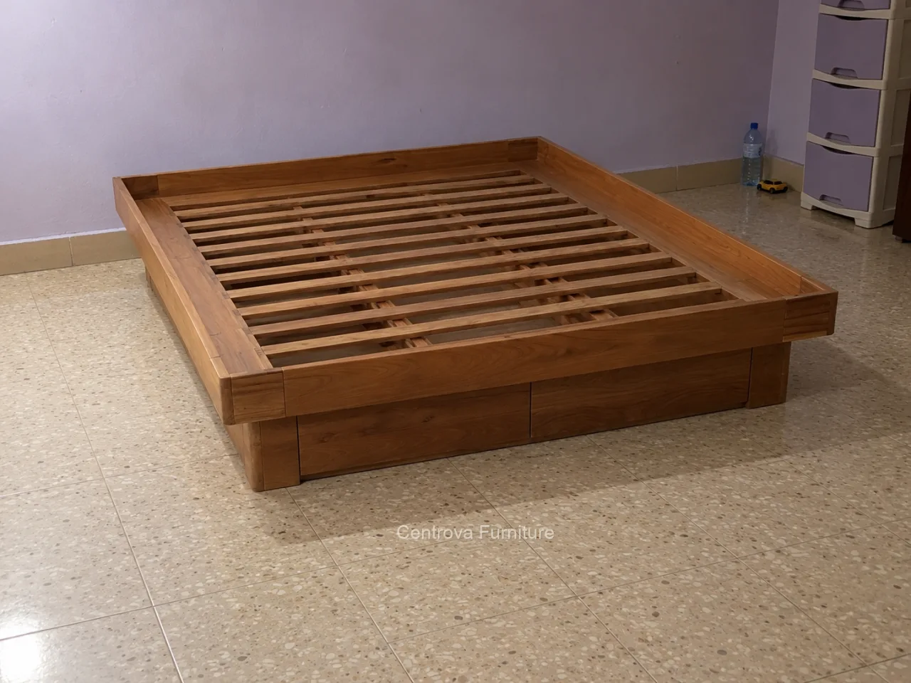 Dipan jati rendah tanpa sandaran dalam kamar sederhana dengan lantai teraso.