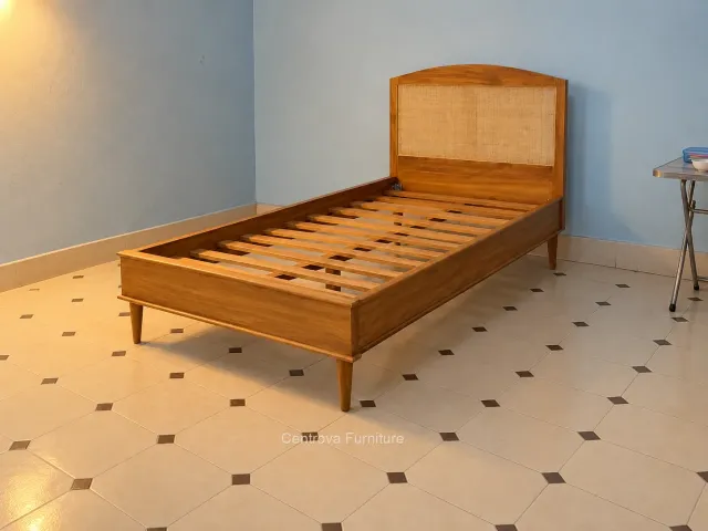 A single teak bed with a woven cane headboard in a simple bedroom under warm household lighting.